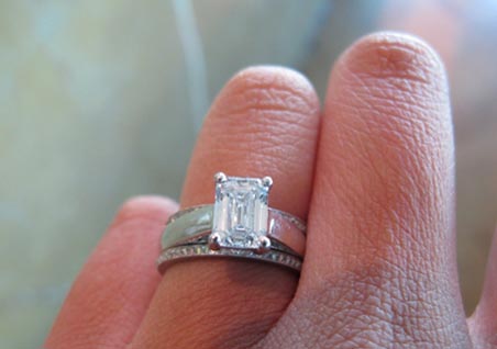 Emerald cut solitaire engagement ring with diamond wedding bands on hand