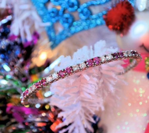 Pink sapphire and diamond bangle placed on a white Christmas tree.