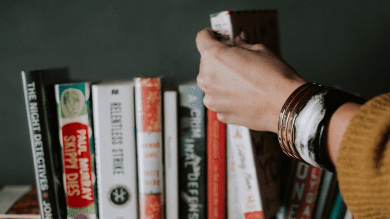 Hand reaching for books Photo by Christin Hume on Unsplash.