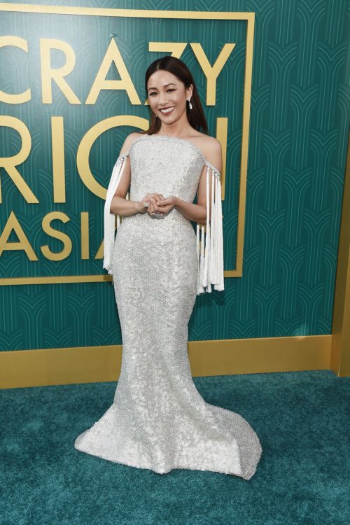 Constance Wu in a glittering crystal gown in front a green sign that reads "Crazy Rich Asians" in gold text