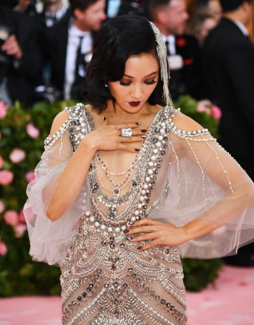 Constance Wu in silver flapper style gown covered in inlayed pearls, with a giand diamond cocktail ring and dark makeup at the 2019 Met Gala