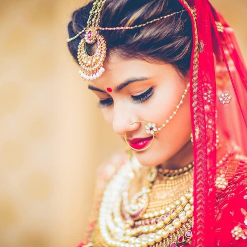 Indian bride with maang tikka, nosering, several necklaces, with a red veil