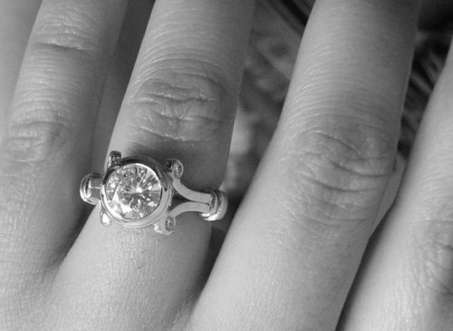 black and white image with a hand that has a diamond engagement ring on it in an ornate setting