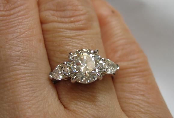 diamond engagement ring large center stone with 2 side stones, on a finger