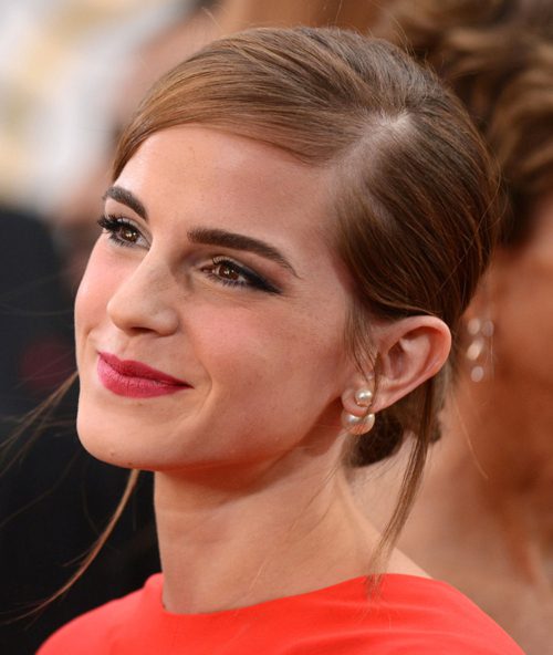 Emma Watson close up, hair pinned up, in red top with pearl front back earrings. 