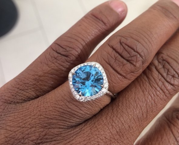 A cobblestone walkway under a hand aimed down with a stunning blue stone in white diamond prongs and halo. 