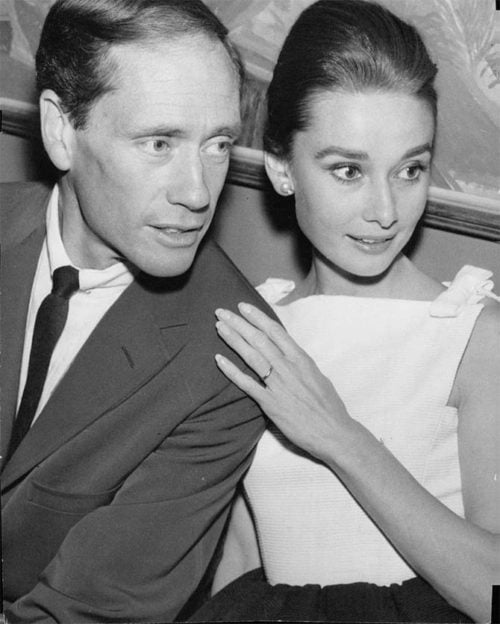 Audrey Hepburn and Mel Ferrer, image is greyscale, he is on the left in a suit and is slightly balding. Audrey is on the right, he hair is in an updo, she is wearing a white sleeveless top, her hand is on his shoulder and her wedding band is visible.