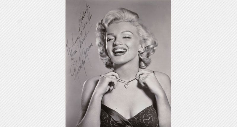 Marilyn Monroe in grey scale, wearing the Moon of Baroda and lifting it to show it. Her autograph is to the left of her head, along with “To Meyer Thanks for the chance to wear the Moon of Baroda.” in her handwriting.