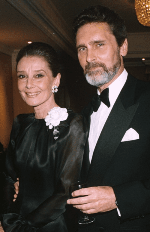 Robert Wolders and Audrey Hepburn both dressed in black tie on a black background.