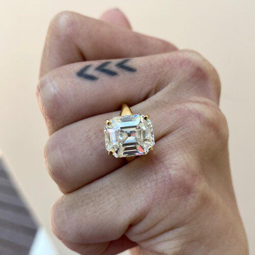large elongated asscher diamond on a yellow gold band on a hand. One finger has a tattoo of 3 chevrons.