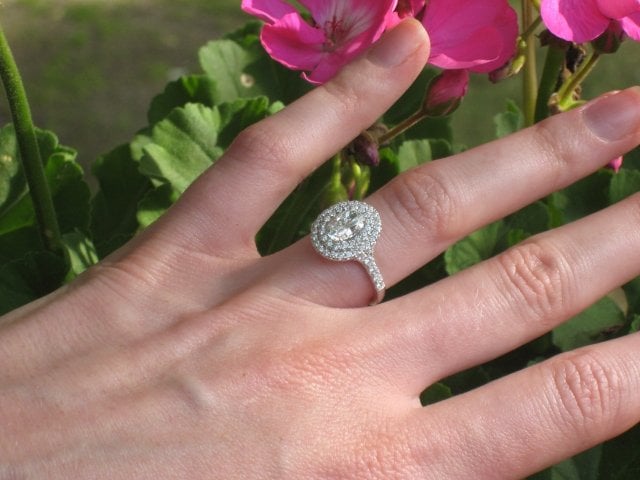 A long fingered hand with a double haloed oval diamond ring.