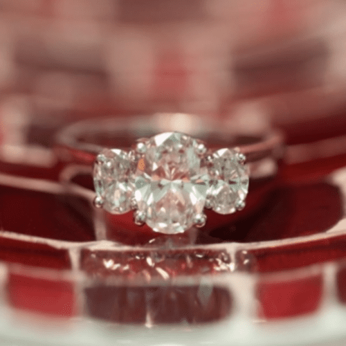 three-stone oval diamond ring set on glass that looks like red bricks