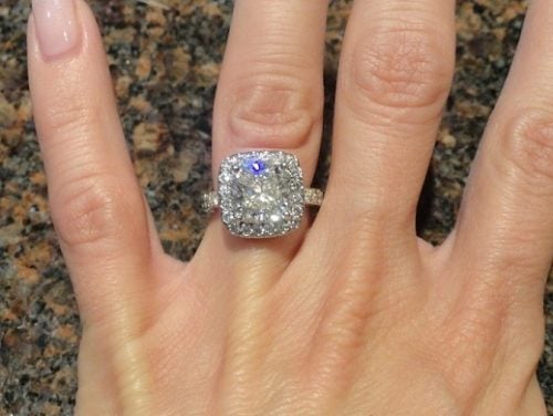 4 fingers held over a countertop with a stunning cushion modified brilliant diamond ring.