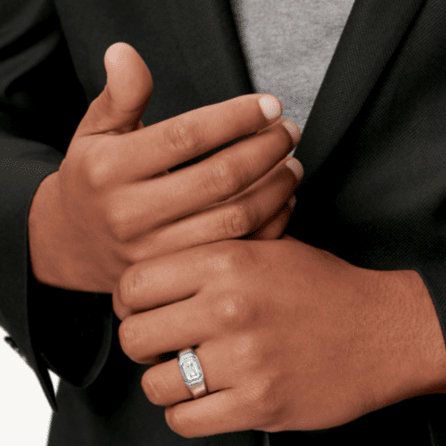 brown men's hands in front of a suited chest with a stunning men's ring on the ring finger with a large diamond.