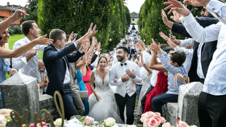 bride and groom run through a gauntlet of their friends and family all standing within a hedgerow with arms uplifted in cheer as the bride and groom run through with linked arms.