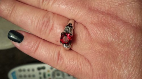 bright red garnet ring with diamond baguette side stones on a hand with one darkly polished nail showing