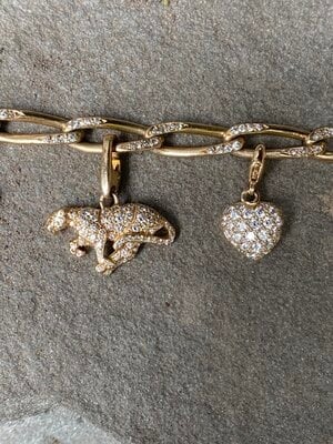 a panther charm and a heart shaped charm on a cartier diamond bracelet. charms are gold with diamonds