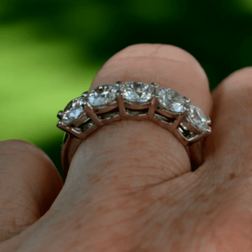 3/4 profile of a five-stone diamond ring on a finger with a muted green background