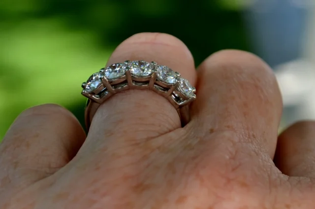 3/4 profile of a five-stone diamond ring on a finger with a muted green background