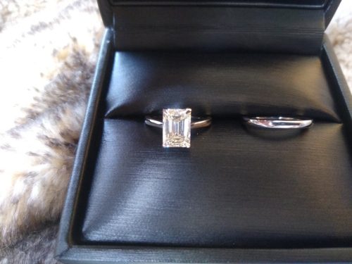 Black ring box with a silver wedding band and an emerald cut diamond ring.