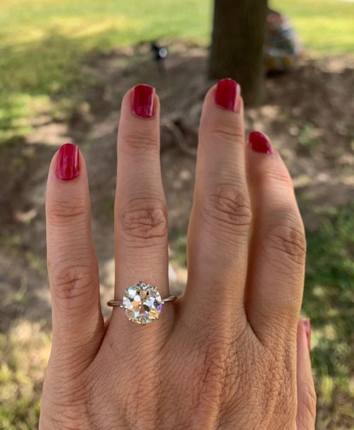 Large disco ball style diamond ring on a feminine hand with red painted nails. green grass in the background.