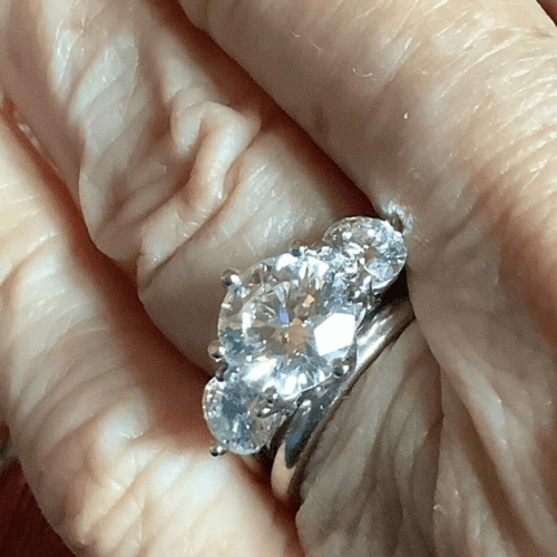 A close up of a part of a hand with a large diamond three-stone ring on the ring finger.