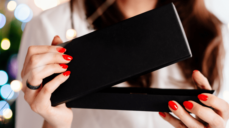 feminine hands opening a black gift box.