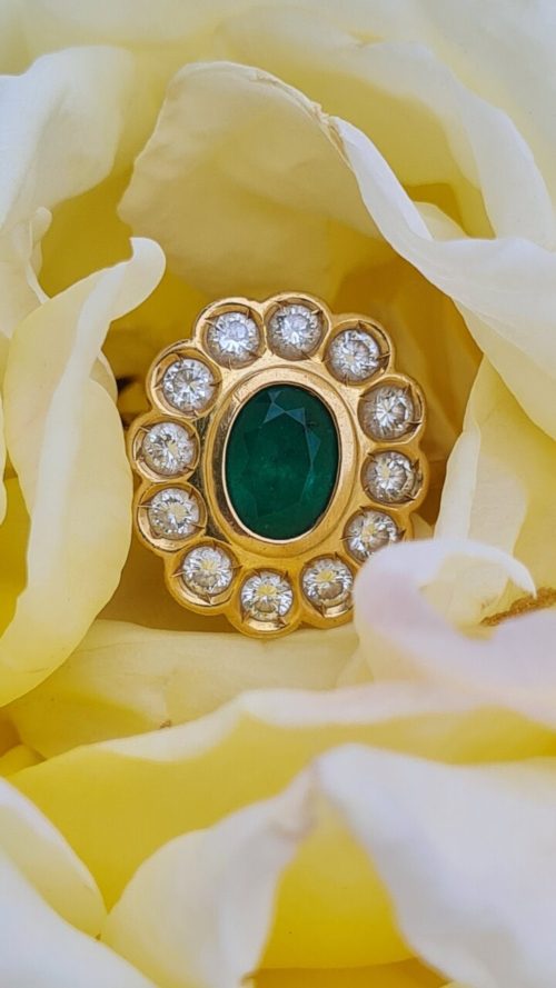 Oval floral cluster with diamonds as petals and an emerald center. Ring is sitting within a yellow and white flower.