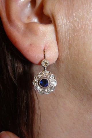 Diamond and sapphire floral earrings. Hanging from an ear lobe.