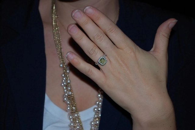Chest of a woman holding her hand in front of her displaying her yellow diamond in white diamond halo engagement ring. Her face is not visible.