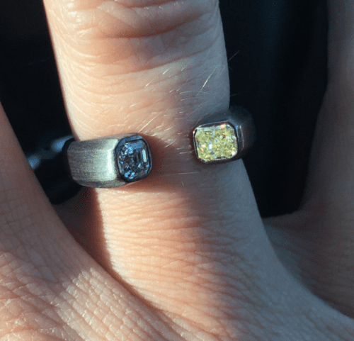 A masculine finger with a dar 3/4 ring with a white diamond set in one end and a yellow diamond set in the other.