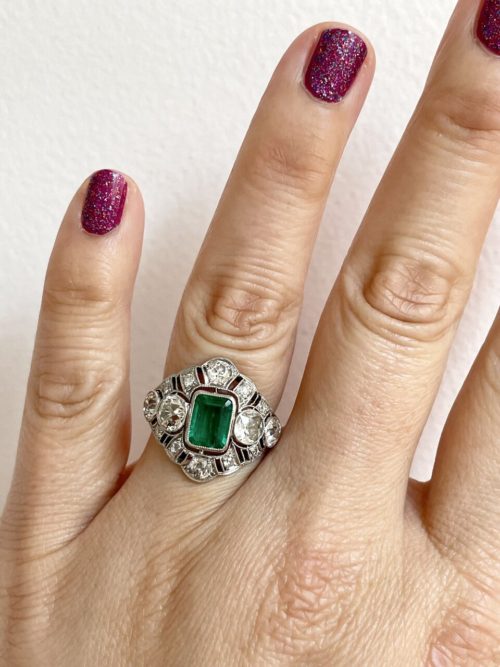 A hand with a large emerald and diamond dinner ring.