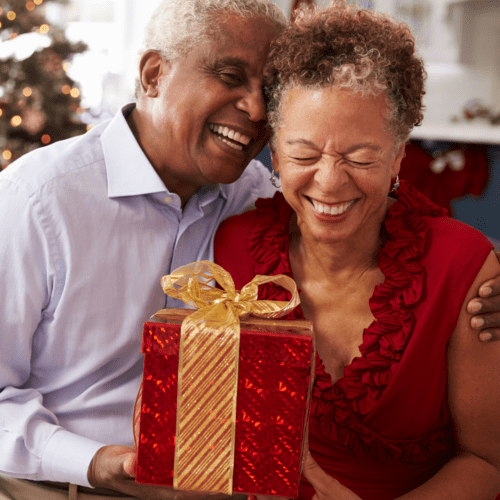 A couple happily embracing with a gift, they seem to be laughing.