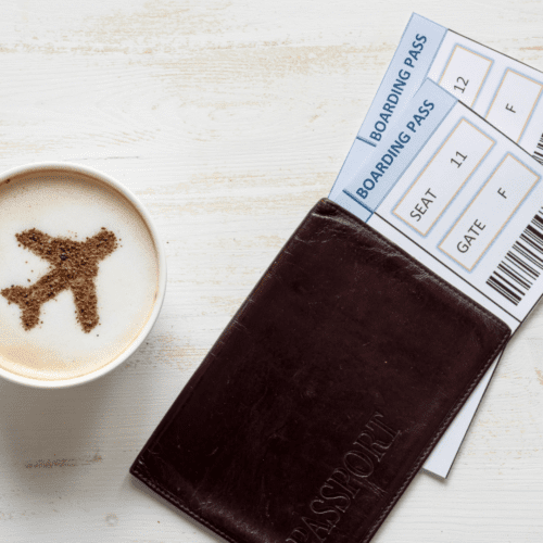 A pair of plane tickets in a small folder and a latte with a coooa powder airplane on the top.