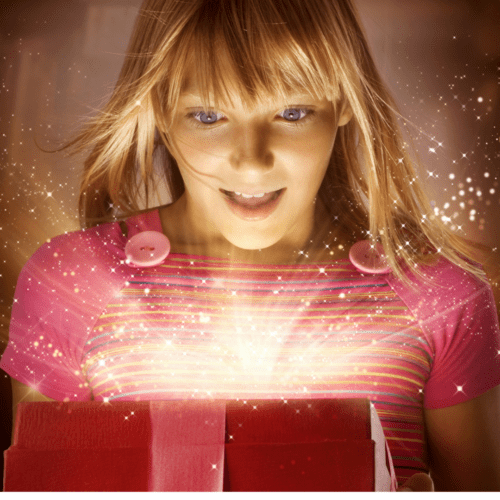 A blonde young woman is looking down into an open gift box with rays of light shining out of it. 