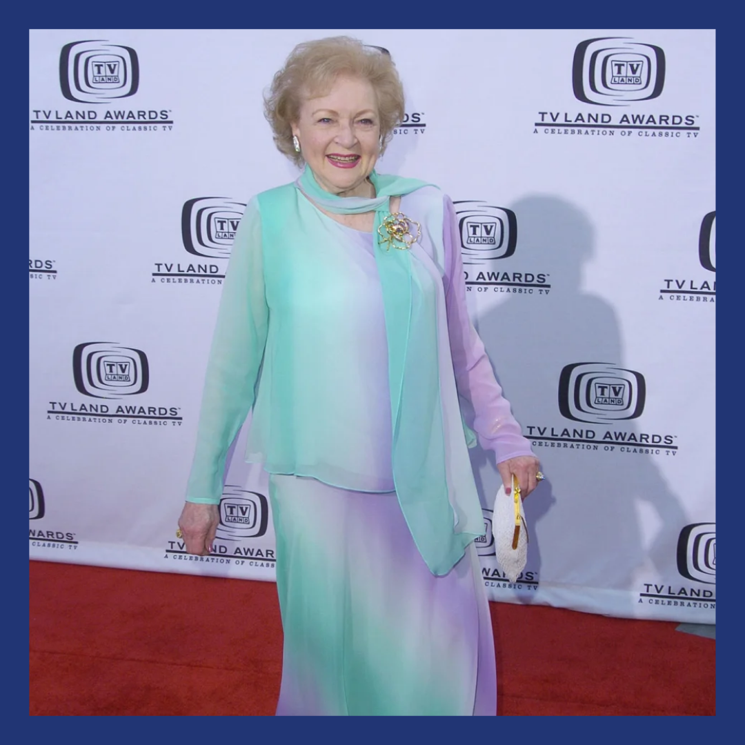 Older woman on a red carpet in a pastel colored dress.