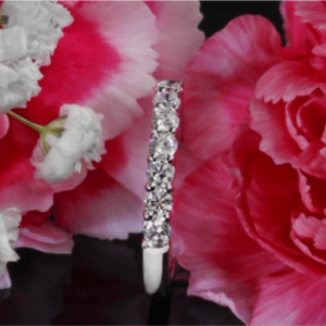 Seven stone diamond wedding band surrounded by pink flowers on a black background.