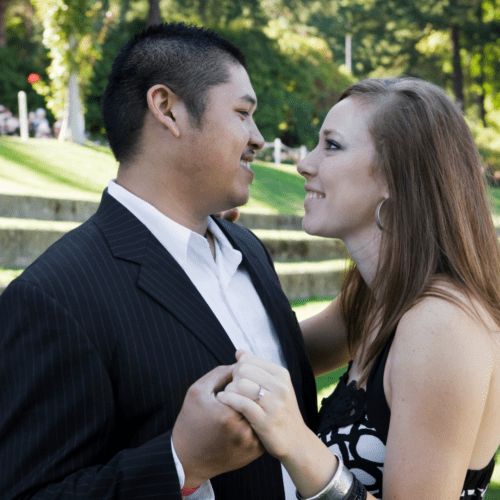 A couple dressed up standing outdoors embraced.