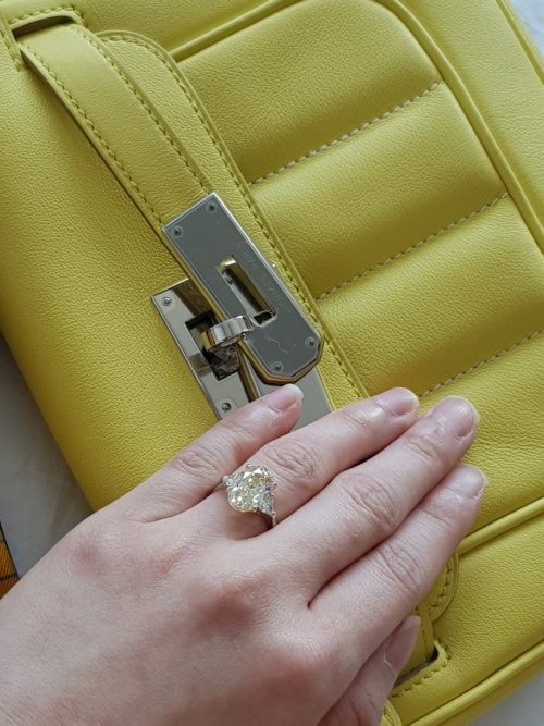 Hand with yellow diamond ring on top of yellow Hermés purse.