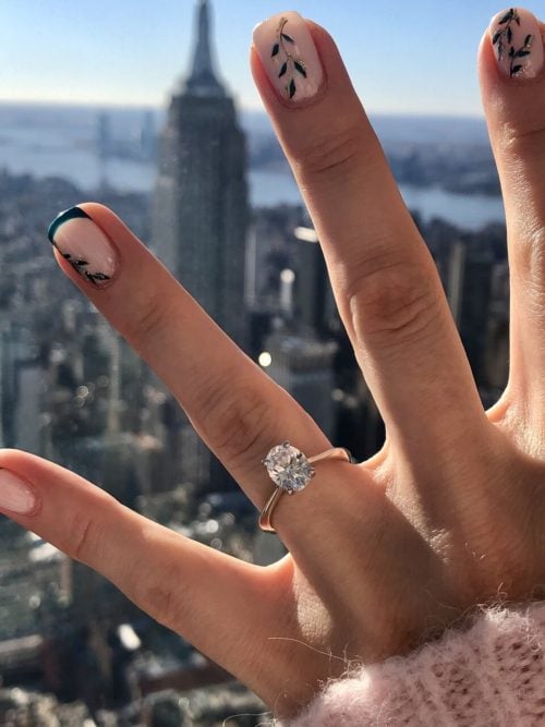 A hand with a fabulous vine manicure and an oval engagement ring with NYC in the background.