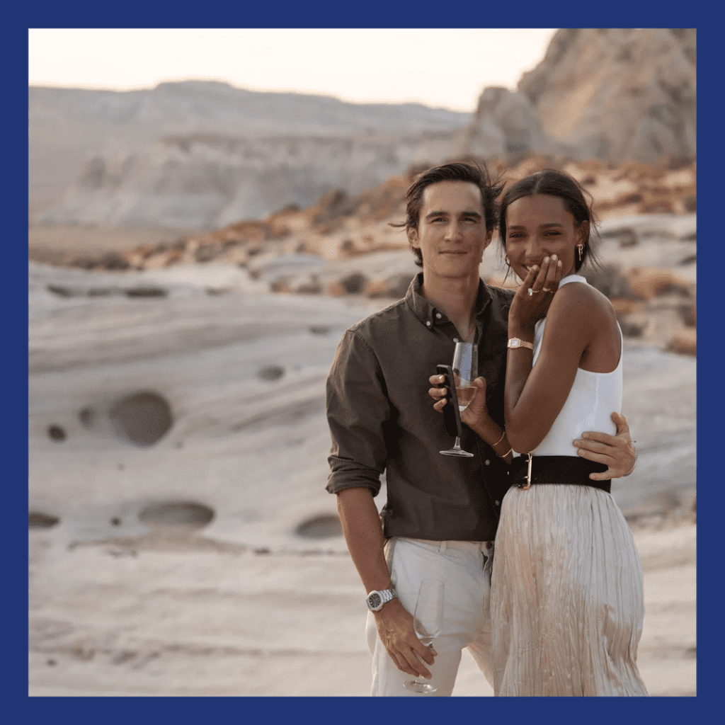 Woman of color and a caucasian man standing in the desert at the base of a mountain.