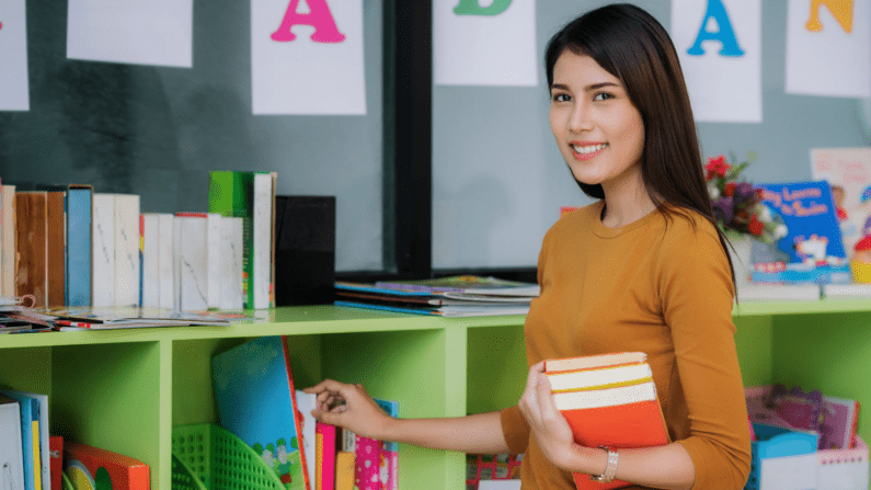 Asian woman standing in what appears to be a children's classroom.