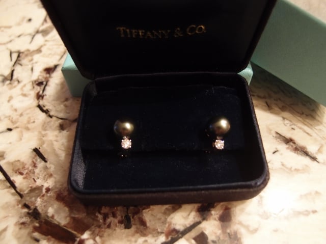 Dark pearl and diamond earrings in a box on a counter.