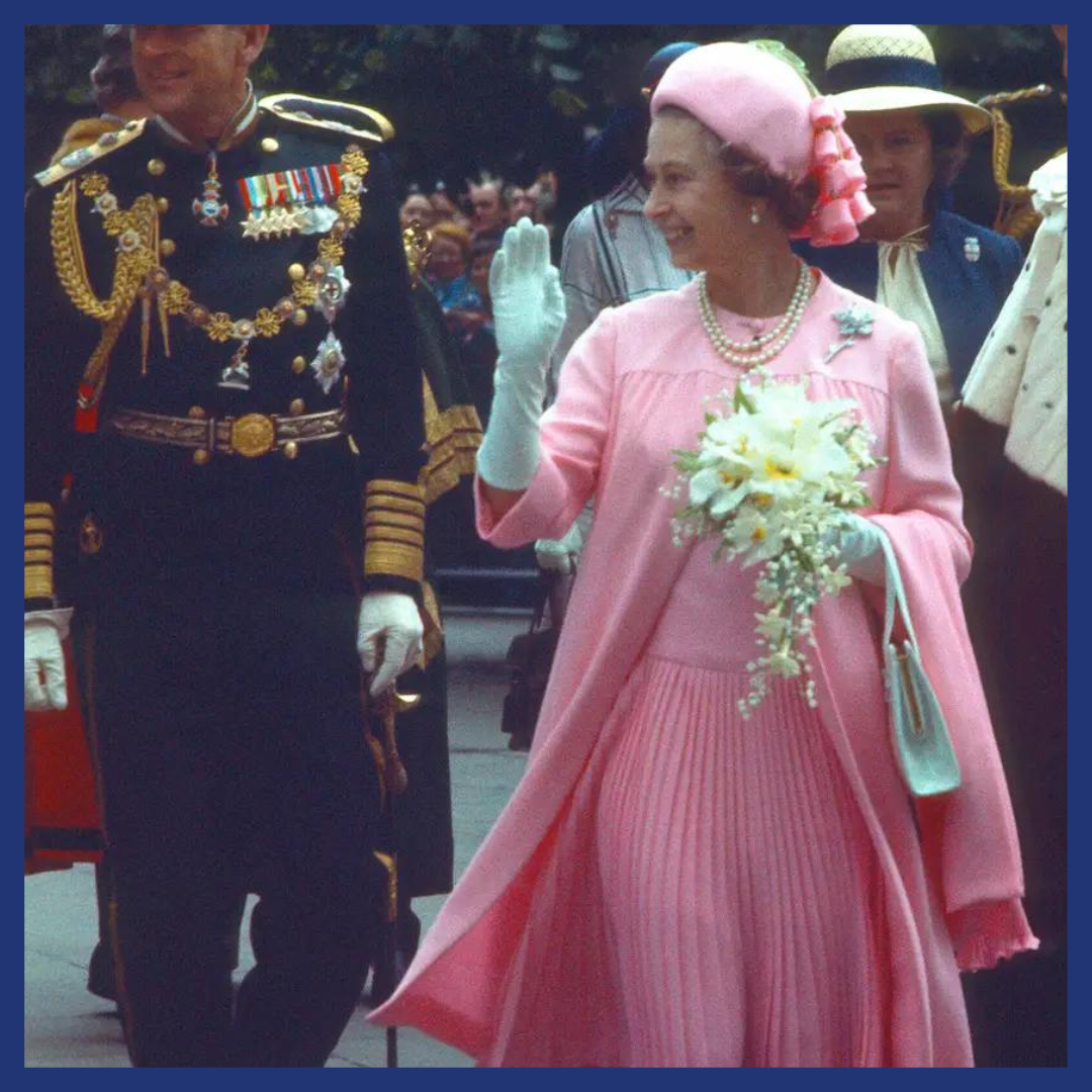 Queen Elizabeth II wearing a bubblegum-pink pleated dress with a flowing cape-like coat. 