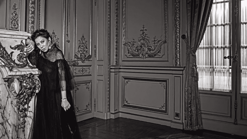 black and white image of a woman leaning on a mantle in a decadently decorated room.