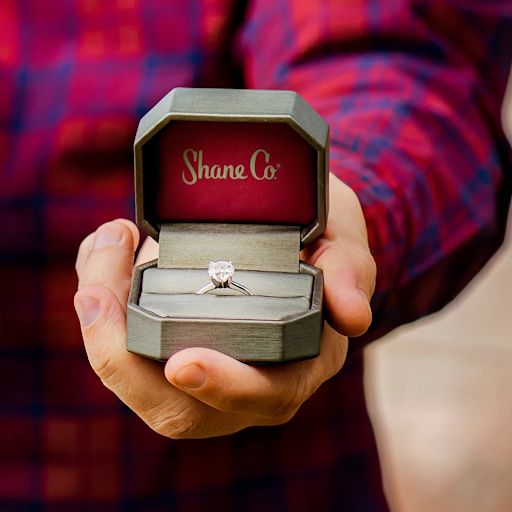 Man holding Shane Co silver ring box with solitaire engagement ring 