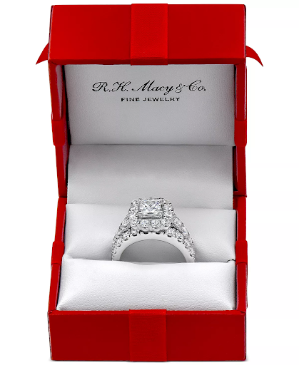 Macy's red ring box, with a decorative ribbon placed on top. Inside is a halo engagement ring.