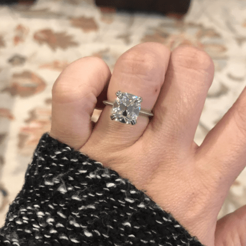 Diamond ring on a hand with a black sweater sleeve over the wrist.