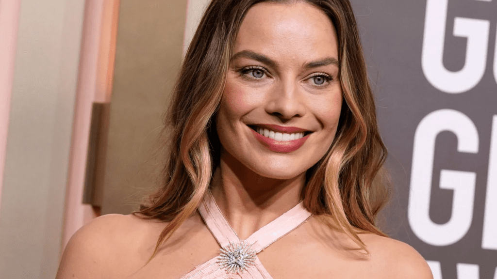 Blonde woman on the red carpet in a pink halter top dress and a diamond star brooch