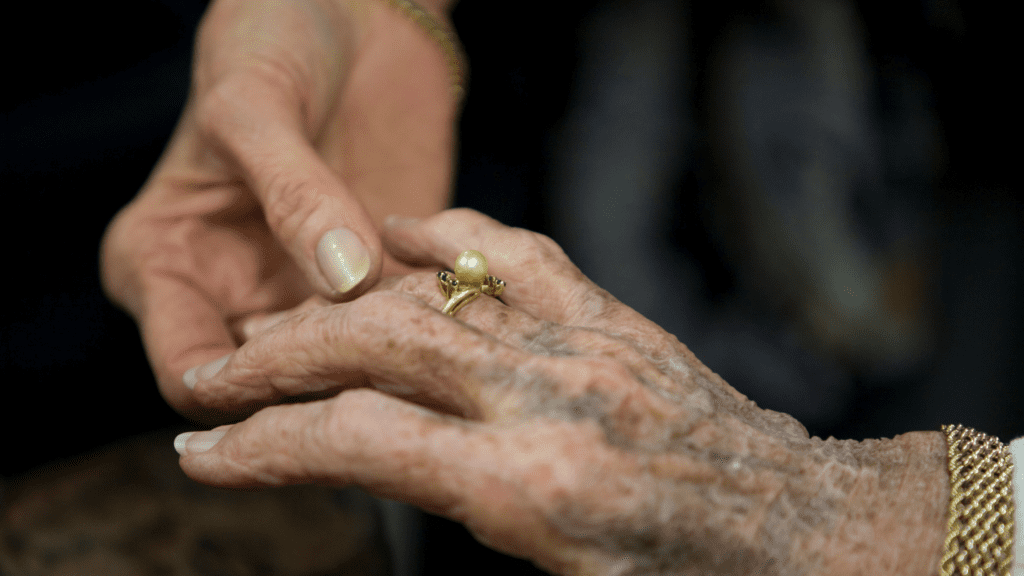 Young hand holds an older hand with a large pearl ring